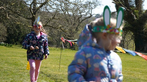 Two girls wearing bunny ears and balancing eggs on wooden spoons